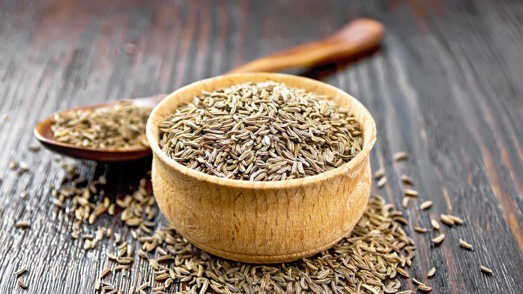 Cumin seeds in a bowl, spoon and on table against the background of wooden board